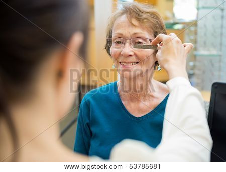Female optician measuring mature woman's eyeglasses in store