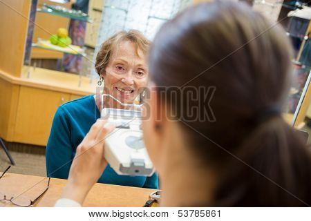 Senior woman in eyeglass store with optometrist reading pupilometer