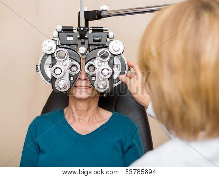 Female ophthalmologist using phoropter to check a senior woman's eyes