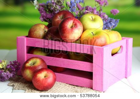 Juicy apples in box on white wooden table on natural background