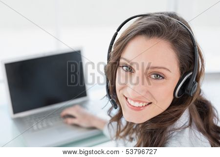 Close up portrait of a smiling businesswoman wearing headset in front of laptop in office