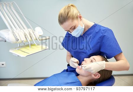 people, medicine, stomatology and health care concept - happy female dentist with mirror and probe checking patient girl teeth up at dental clinic office