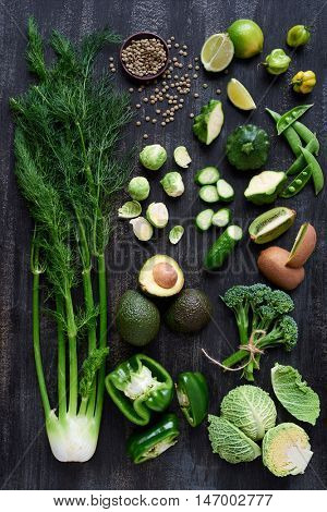 Variety of green vegetables produce on dark background from overhead, broccolini, fennel, avocado, brussel sprouts, kiwi, pepper, peas, lime part of flat lay series