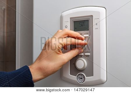 Men hand regulate temperature on 50 degree in control panel of central heating.