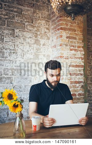 Young beard man is speaking with his family using web camera and messanger on the laptop while sitting in a nice loft cafe. Computer and communication concept