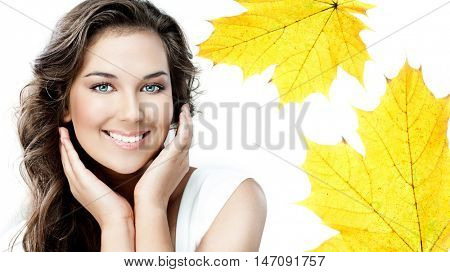 beauty portrait of attractive caucasian smiling young woman brunette isolated on white studio shot  toothy smile face looking at camera hands yellow marple autumn leaves