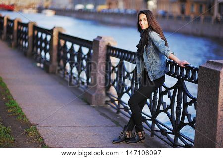 Beautiful Girl In Blue Jeans Jacket And Scarf Straightens Hair Standing Near The Parapet On The Emba