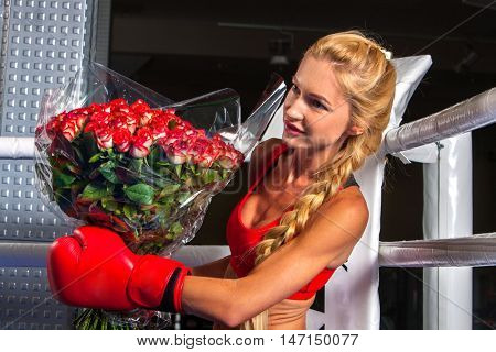 Boxing girl wearing boxing red gloves with presented bouquet flowers sitting in corner of boxing ring.