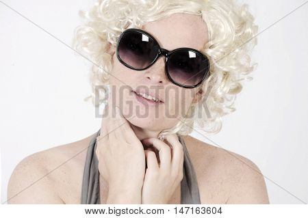 Beautiful young woman is wearing sunglasses and a blonde wig in Marylin style. Studio shot with light background. Isolated.