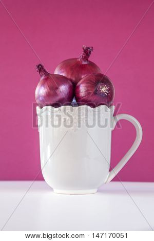 Group of three onions in mug on purple