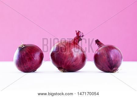 Group of three red onions on violet