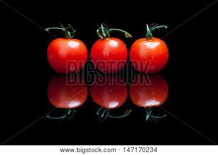 Three tomatoes on a black shiny background