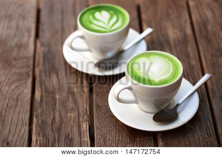Two cups of matcha latte with latte art on wooden table.