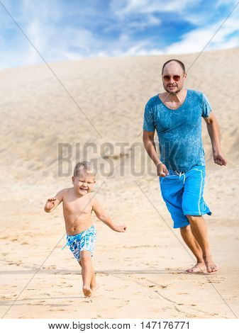 Son and father are running on the beach 