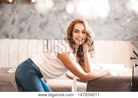 Smiling beautiful woman 20-24 year old with curly hair posing in cafe. Looking at camera. 20s.
