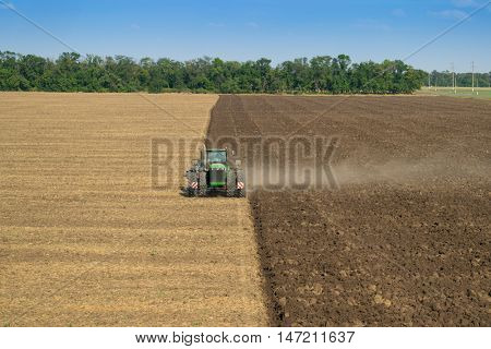 KRASNODAR REGION, RUSSIA - AUG 19, 2015: Modern green tractor plows big field, In 2015 in Krasnodar region yields reached record level - 58.4 centners per hectare