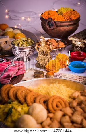 oil lamp or diya with crackers, sweet or mithai, dry fruits, indian currency notes, marigold flower and statue of Goddess Laxmi on diwali night while laxmi pujan or pooja