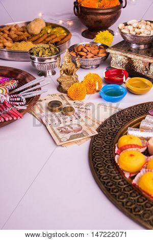 oil lamp or diya with crackers, sweet or mithai, dry fruits, indian currency notes, marigold flower and statue of Goddess Laxmi on diwali night while laxmi pujan or pooja