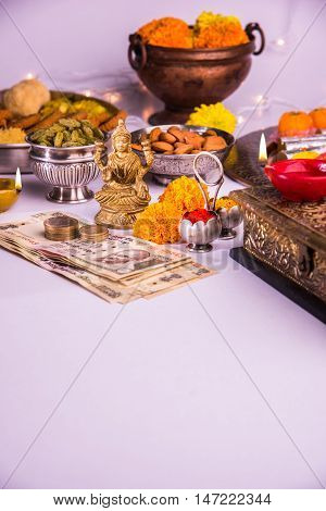 oil lamp or diya with crackers, sweet or mithai, dry fruits, indian currency notes, marigold flower and statue of Goddess Laxmi on diwali night while laxmi pujan or pooja