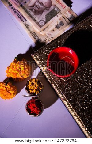 oil lamp or diya with crackers, sweet or mithai, dry fruits, indian currency notes, marigold flower and statue of Goddess Laxmi on diwali night while laxmi pujan or pooja