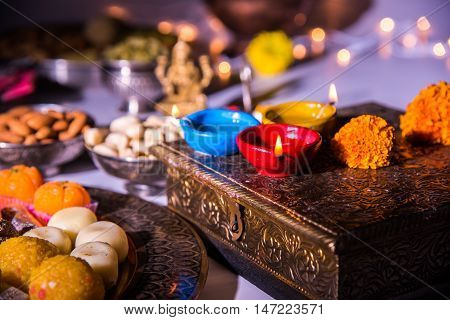 oil lamp or diya with crackers, sweet or mithai, dry fruits, indian currency notes, marigold flower and statue of Goddess Laxmi on diwali night while laxmi pujan or pooja