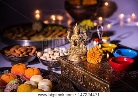 oil lamp or diya with crackers, sweet or mithai, dry fruits, indian currency notes, marigold flower and statue of Goddess Laxmi on diwali night while laxmi pujan or pooja