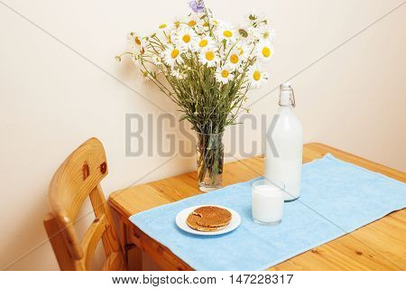 Simply stylish wooden kitchen with bottle of milk and glass on table, summer flowers camomile, healthy foog moring concept country interior
