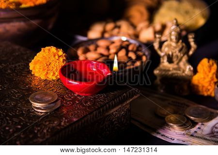 oil lamp or diya with crackers, sweet or mithai, dry fruits, indian currency notes, marigold flower and statue of Goddess Laxmi on diwali night