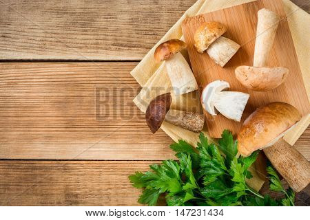 Boletus mushroms with parsley on cuting board on rustic wooden background. Top view.