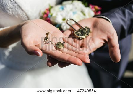 Decorative wedding lock and keys with coulomb in hands of newlyweds.