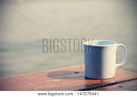 Coffee cup on wooden floor and river (vintage background)
