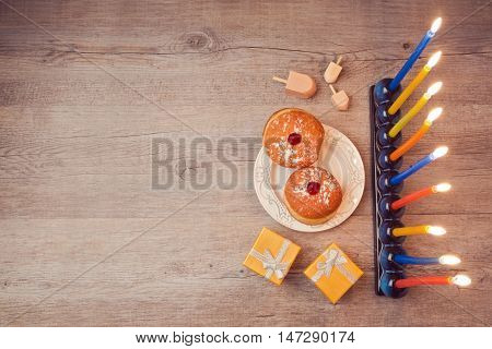 Hanukkah creative background with menorah and sufganiyot on wooden table. View from above