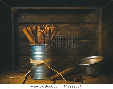 Cinnamon sticks in tin can and ground cinnamon in strainer, rustic wood bacground, selective focus, copy space