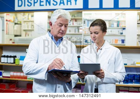 Pharmacists discussing on digital tablet and clipboard in pharmacy