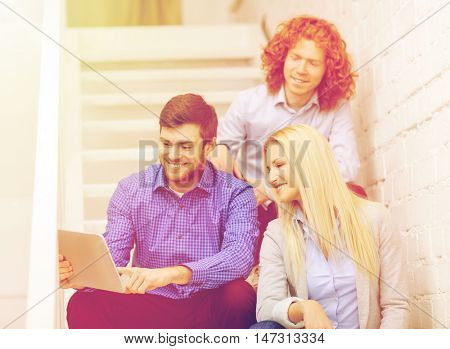 business, technology and startup concept - smiling creative team with tablet pc computer sitting on staircase