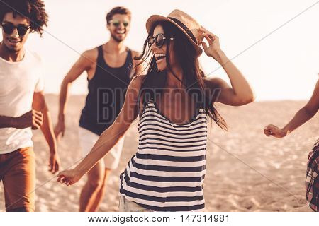 Enjoying youth and freedom. Group of young cheerful people running along the beach and looking happy