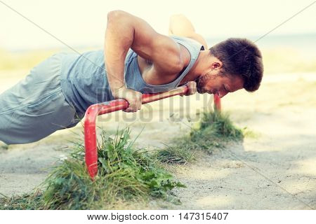 fitness, sport, exercising, training and lifestyle concept - young man doing push ups on horizontal bar outdoors