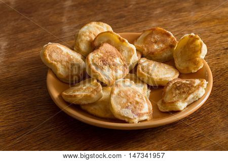 Heap of olady (traditional ukrainian pancakes) in orange plate on wood table.