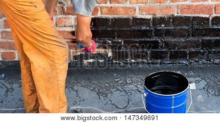 Roofer covered brick wall bitumen primer for improving adhesion during surfacing contiguity with rolled waterproofing during the installation of flat roof.