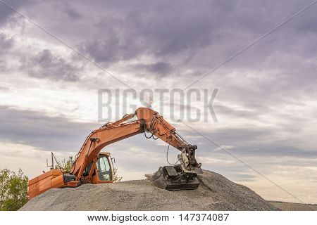 Hydraulic excavator climbed on a ballast pile - Heavy orange excavator with big bucket working on top of a ballast pile.