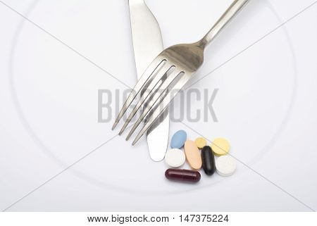 Colorful capsules and pills on plate with fork knife - healthy diet.