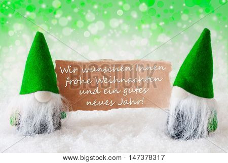 Christmas Greeting Card With Two Green Gnomes. Sparkling Bokeh And Natural Background With Snow. German Text Weihnachten Und Ein Frohes Neues Jahr Means Merry Christmas And A Happy New Year