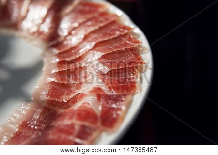 Half decorated arrangement of iberian cured ham on plate isolated over black background