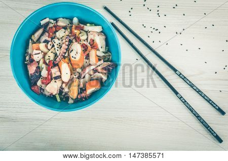 Fresh salad with seafood tomatoes and celery in a blue bowl on wooden background. Asian salad with squid octopus shrimp mussel and black seazsame seeds. Asian food. Seafood concept. Top view.