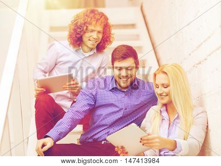business, technology and startup concept - smiling creative team with tablet pc computer sitting on staircase