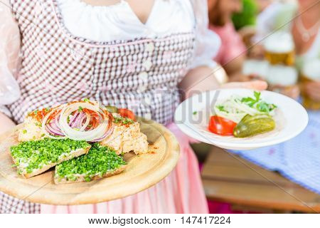 Waitress serving Bavarian food in beer garden, cold cuts, bread and obazda 