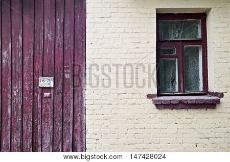 Old brick yellow wall with window and vinous wooden fence close-up.