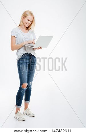 Full length portrait of a happy woman using laptop computer isolated on a white background