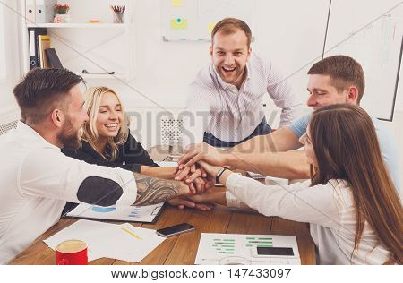 Team put hands together, show connection and alliance. Teambuilding in office, young happy businessmen and women in casual unite hands for teamwork and cooperation at new project.