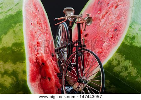 Little model of a retro vintage bicycle near a big cut in half scarlet ripe watermelon